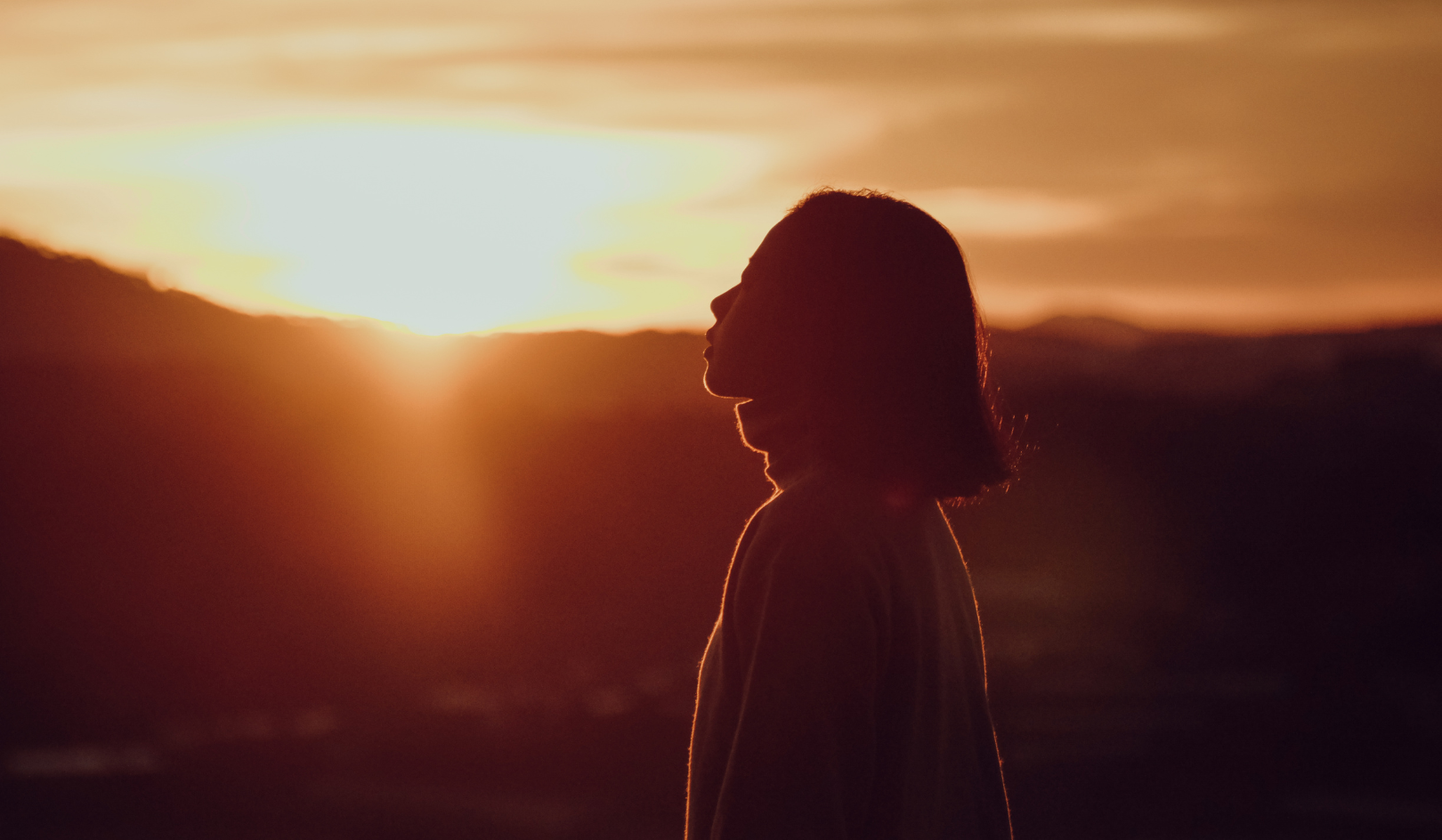 Woman standing outdoors with eyes closed and arms relaxed, symbolizing somatic release and letting go of tension.