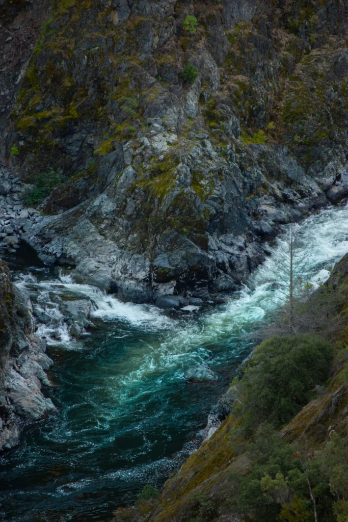 A deep teal river rushing through a moss-covered rocky canyon, water moving freely between stone banks: a visual metaphor for processing grief and letting go.