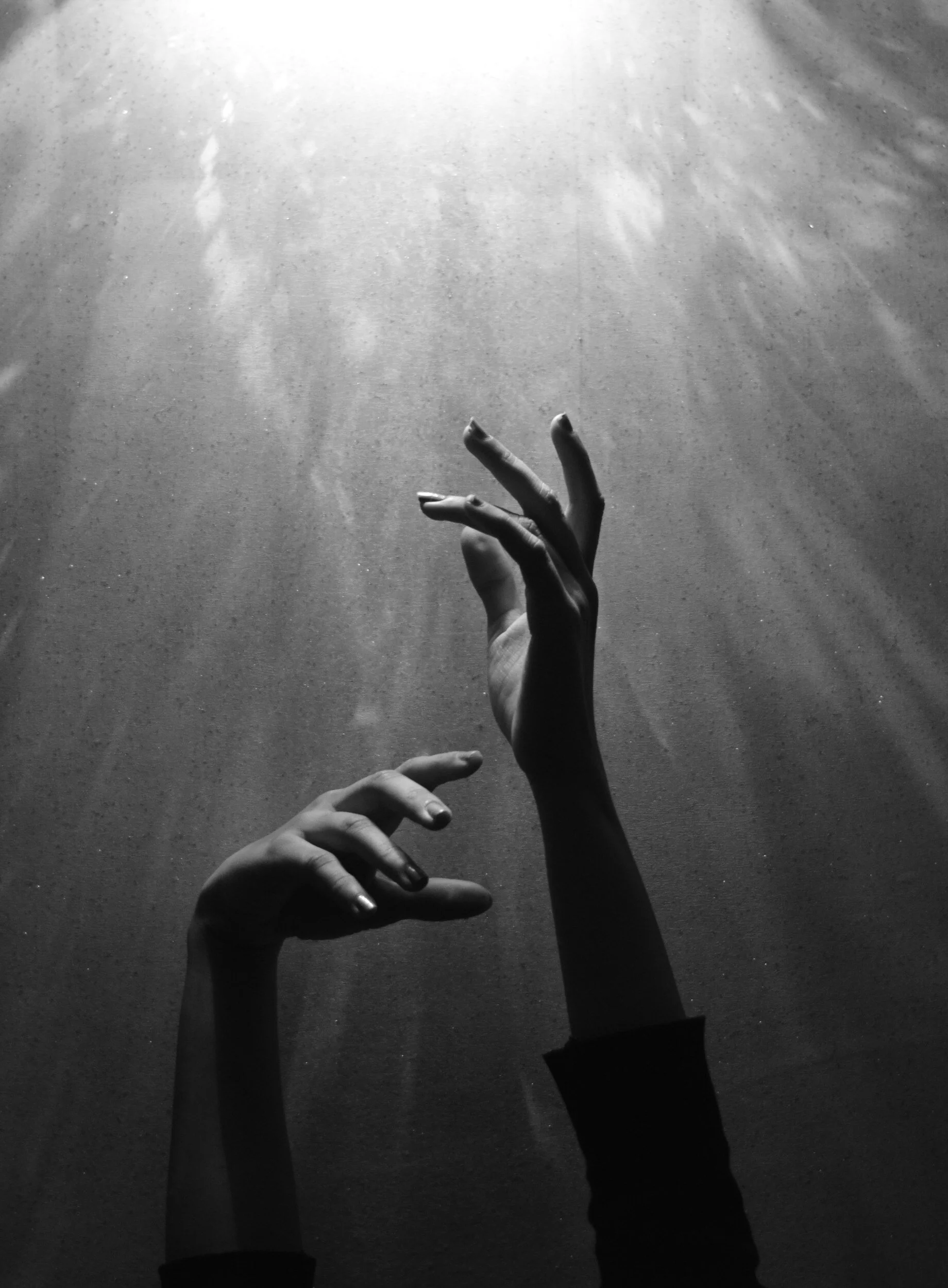 Two hands reaching upward into streaming light against a dark background, fingers open in a gesture of devotion and spiritual intimacy.